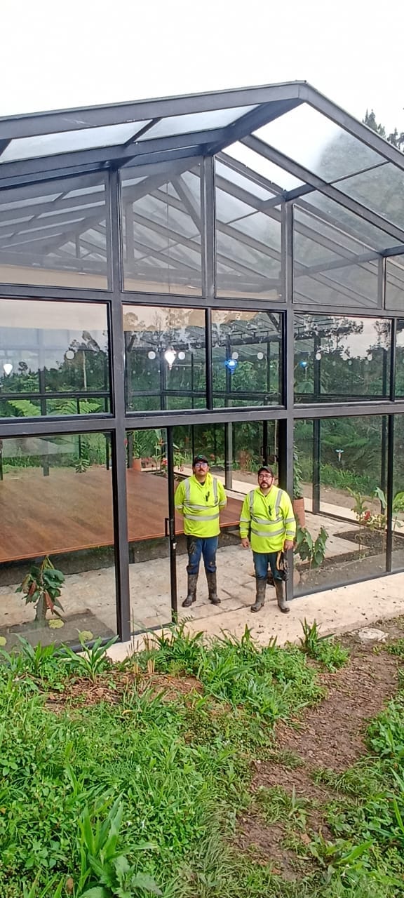 Dos técnicos frente a un invernadero de vidrio y estructura metálica construido en el campo